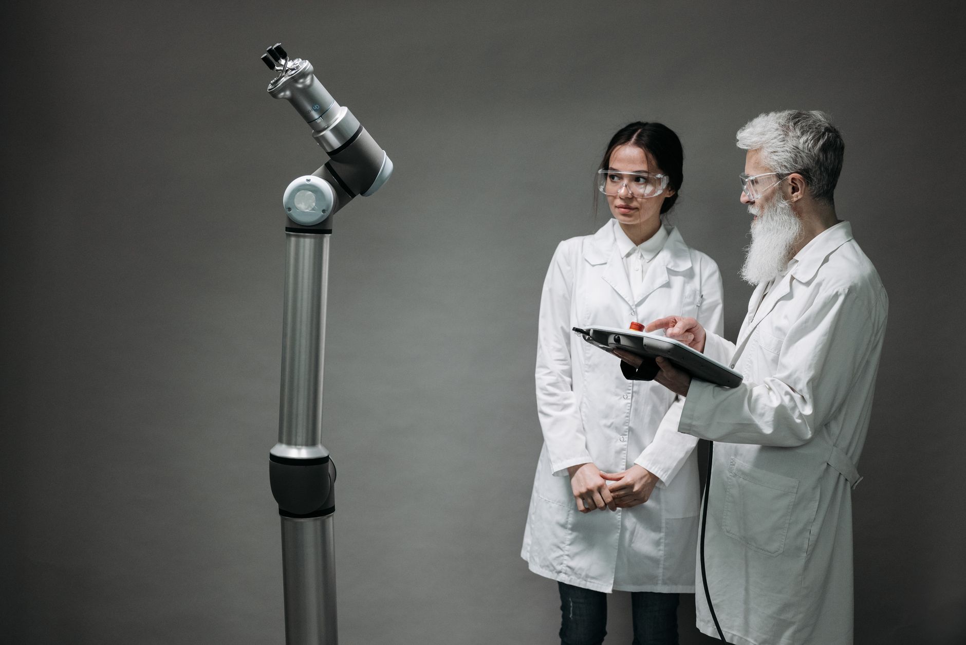 A collaborative robot arm mounted in a factory cell next to an industrial PLC cabinet