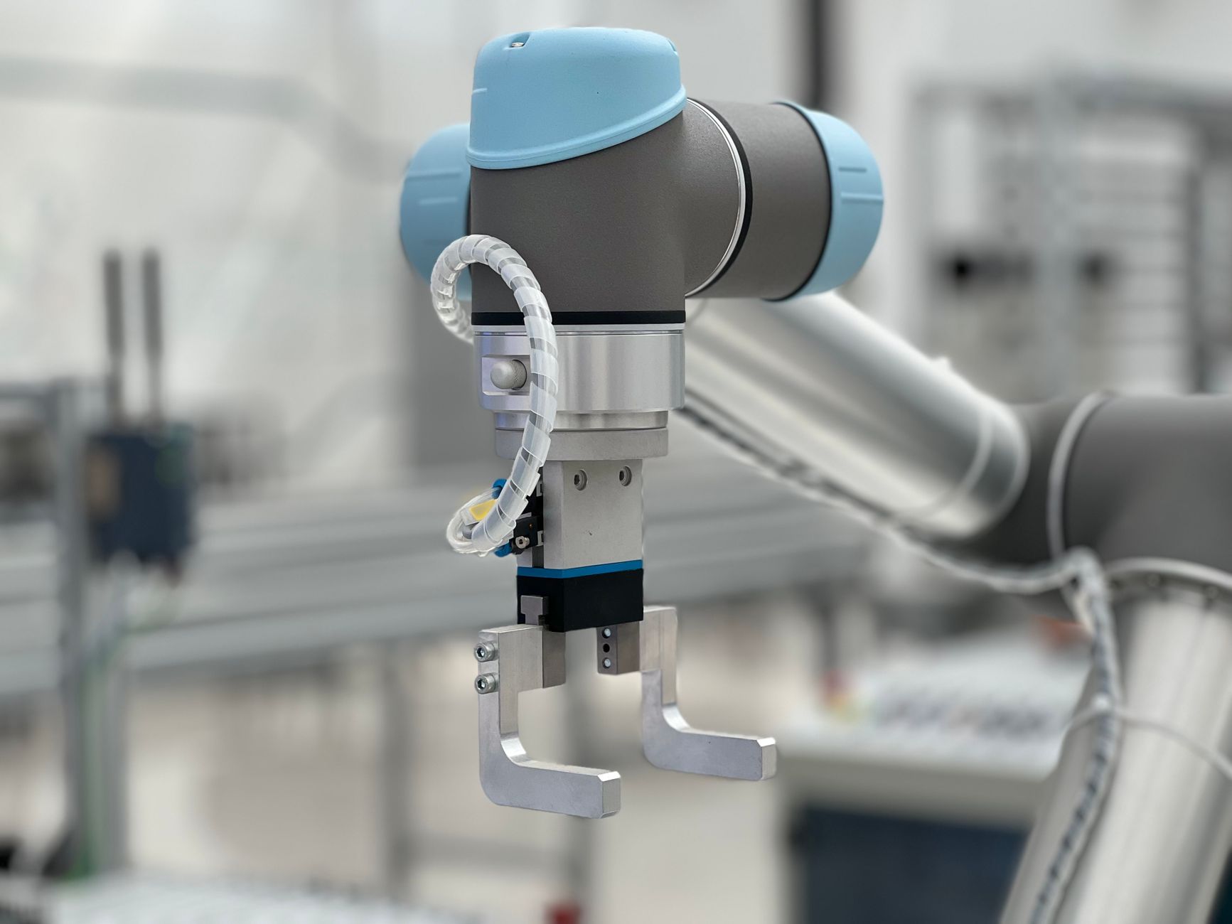 A collaborative robot arm working alongside a caged industrial robot on a factory floor