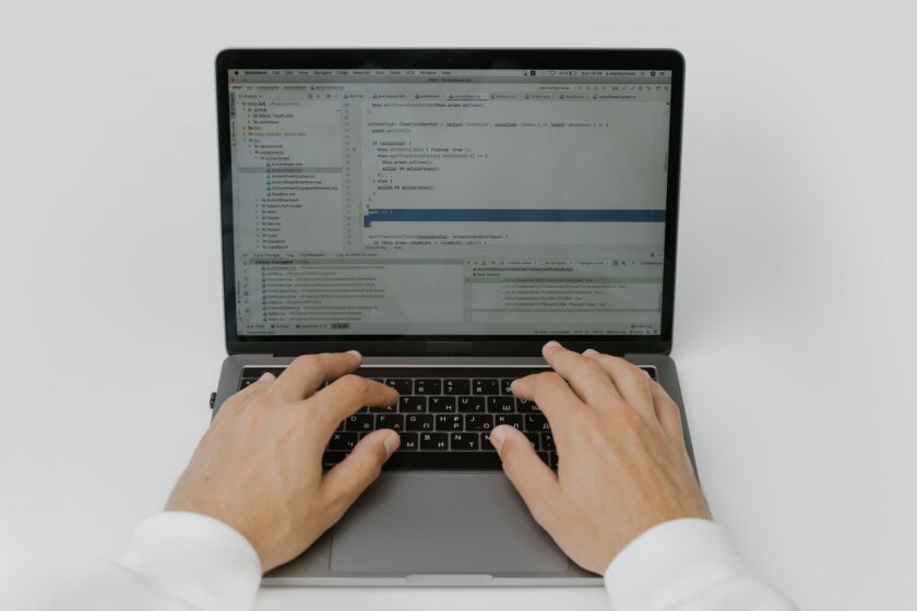 An automation engineer reviewing PLC code on a laptop next to an industrial control cabinet