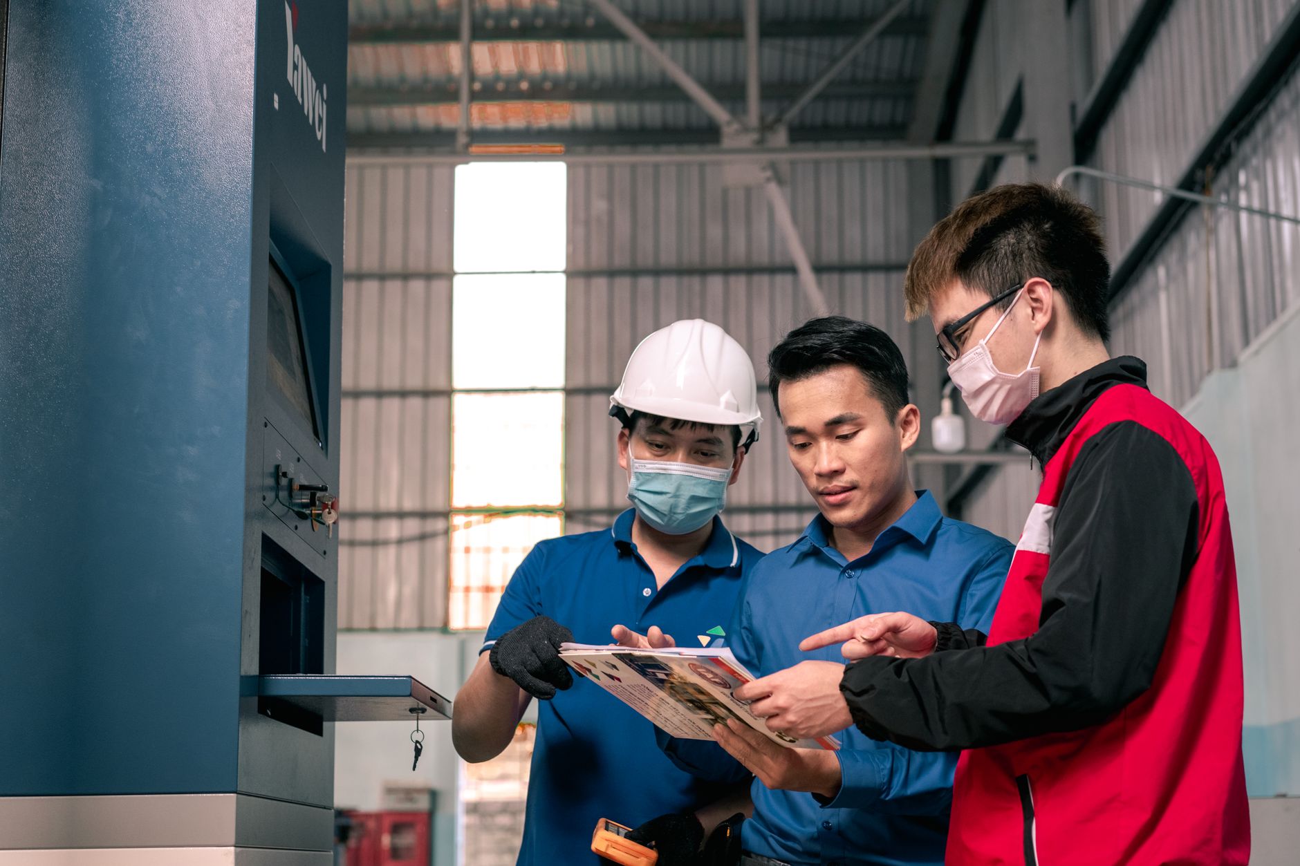 Operators reviewing a digital dashboard during a shift change on a factory floor