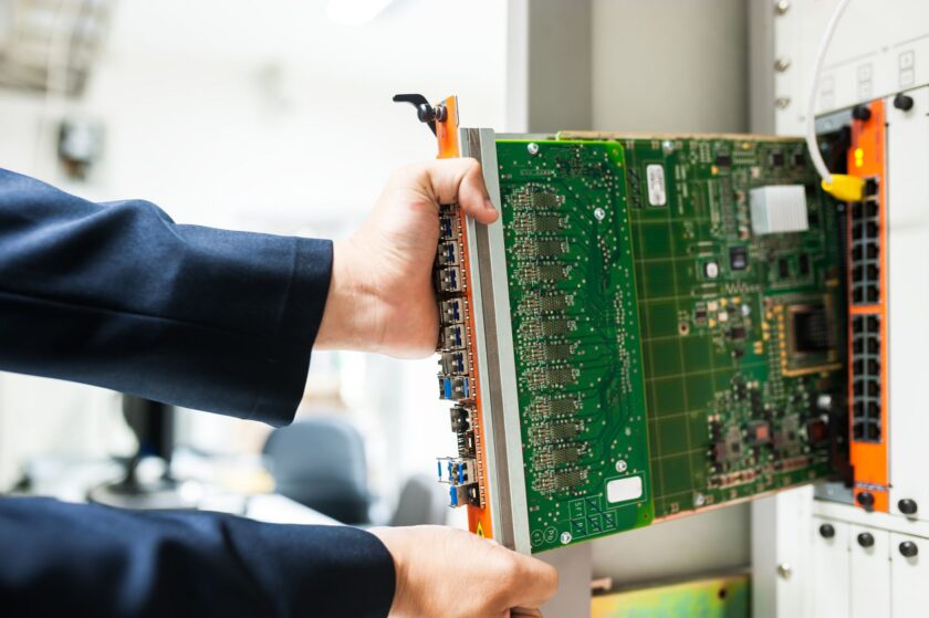 Engineer reviewing industrial control system security data on a laptop near a PLC cabinet