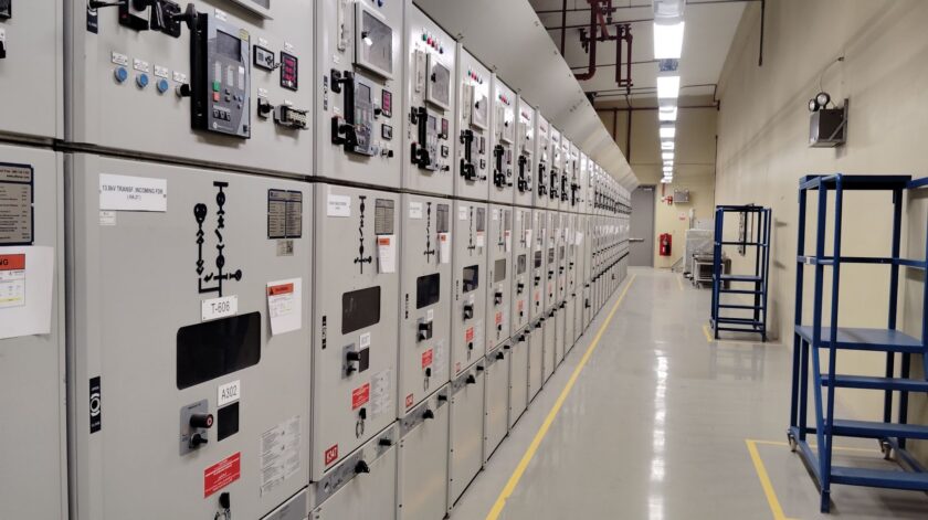 Technician standing before an industrial control panel with PLC and RTU hardware in a manufacturing plant